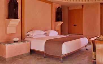 Terracotta-walled bedroom at Amanjena with draped bed and arched doorways.