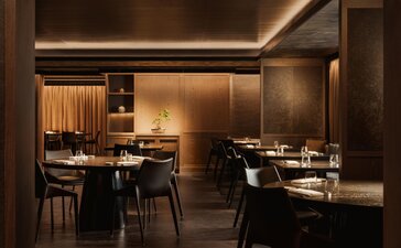 Intimate dining venue at Aman Rosa Alpina with warm lighting, dark wood finishes, and tables set for service.