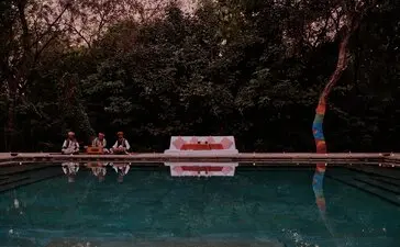 Evening pool dinner with musicians at Aman-i-Khas, India, reflected in still water under night sky.