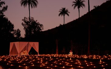 Candlelit dinner setup at Amanbagh beneath a twilight sky, with palm trees silhouetted against mauve hills.