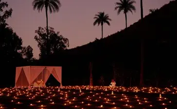 Candlelit dinner setup at Amanbagh beneath a twilight sky, with palm trees silhouetted against mauve hills.