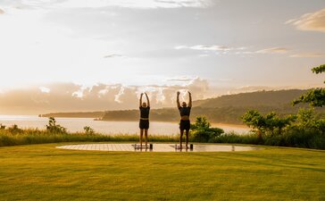Outdoor fitness pavilion at Amanera resort at sunset, with manicured lawn, river and forested hills beyond.