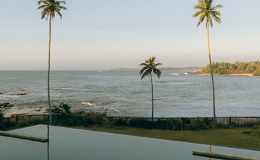 Infinity pool overlooking the Indian Ocean at Amanwella, Sri Lanka, with palm trees reflected in still water.