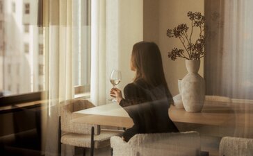 امرأة جالسة على كرسي بجانب نافذة مضاءة بنور طبيعي في شقة بينهاوس بثلاث غرف نوم بفندق أمَان نِيُويُورك.