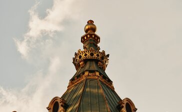 Dettaglio della corona dorata del tetto presso l'hotel Aman New York, con cielo nuvoloso sullo sfondo.