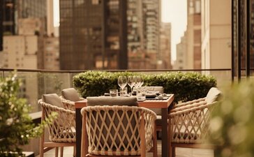 Terrazza dell'hotel Aman New York con sedie in rattan e skyline della città sullo sfondo.