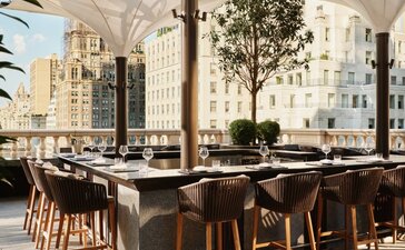 Terrazza bar dell'hotel Aman New York con tavoli all'aperto e vista sulla città.