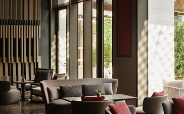 Lounge at Aman New York hotel with floor-to-ceiling windows, contemporary seating and natural light.