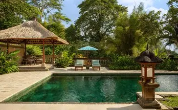 Amandari resort garden pool pavilion with thatched-roof shelters and stone water feature in Indonesia.