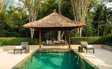 Garden pool pavilion at Amanjiwo with thatched roof, emerald waters, and surrounding greenery in Indonesia.