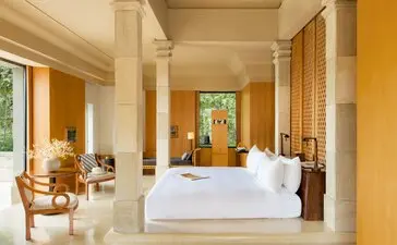 Ruang tidur pavilion dengan tempat tidur berukuran besar, kolom putih, dan pemandangan taman di Amanjiwo resort, Menoreh.
