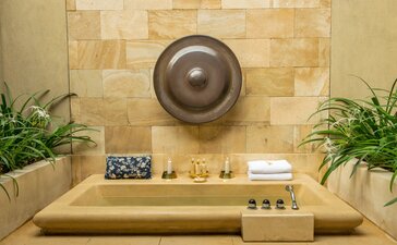 Outdoor bath at Amanjiwo with stone surround, overhead rainfall showerhead, and potted plants on either side.