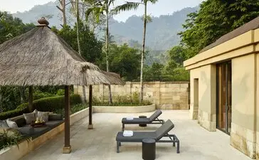 Menoreh Pavilion courtyard at Amanjiwo resort, with stone seating areas, thatched roof structure, and volcanic mountain views beyond.