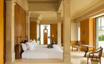 Amanjiwo pavilion bedroom interior with cream walls, wooden screens, and seated area by window.