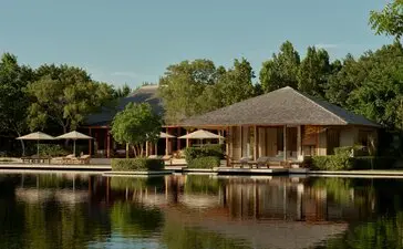 Tranquility Pond at Amanyara, with thatched-roof villas reflected in still water, surrounded by tropical vegetation.