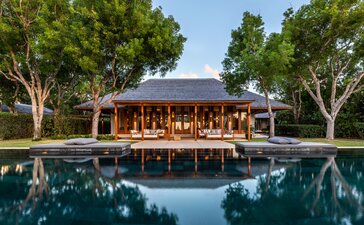 Amanyara six-bedroom villa with wooden pavilion reflected in still pool, framed by tropical trees at dusk.