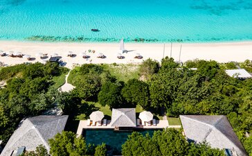Aerial view of a six-bedroom villa at Amanyara with pool, surrounded by tropical vegetation overlooking a turquoise beach.