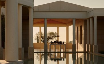 Amanzoe resort entrance at dusk, featuring illuminated wooden doors and columns framing the doorway.