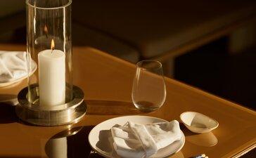 Akari dining venue at Amanzoe, featuring a table setting with a glass of water and plate against warm wooden tones.
