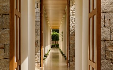 Pathway at Amanzoe resort in Greece, with stone walls and wooden doors leading towards soft golden light.