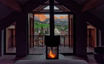 Rosa Alpina suite with open doors framing alpine views, glowing fireplace below.