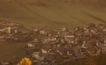 Veduta autunnale della valle di San Cassiano dal resort Aman Rosa Alpina, con larici dorati in primo piano.