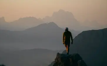 Hiker stood on mountain ridge at sunrise, Aman Rosa Alpina resort, layered peaks in mist below.