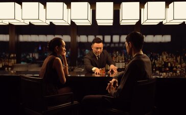Guests conversing at the bar in The Lounge at Aman Tokyo, with warm lighting and a view of the city beyond.