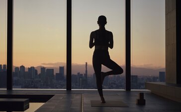 Silhouetted figure practising yoga at Aman Tokyo with Tokyo skyline at sunset visible through floor-to-ceiling windows.