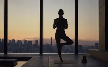Silhouetted figure practising yoga at Aman Tokyo with Tokyo skyline at sunset visible through floor-to-ceiling windows.