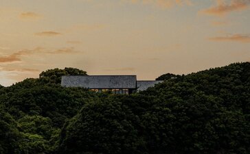 Amanemu resort perched on forested hillside at sunset overlooking calm waters, Japan.