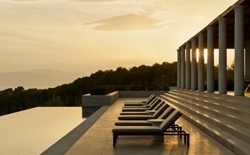 安缦卓熠度假村露台上的躺椅面向宁静的水景，夕阳西下。