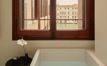 Bathroom with freestanding bathtub and wooden-framed window overlooking Venice buildings at Aman Venice.