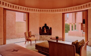 Amanjena pavilion sitting room with terracotta walls, traditional Moroccan arches, and seating areas overlooking the gardens.