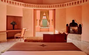 Villa bedroom at Amanjena, Morocco, with terracotta walls and traditional arched doorway.