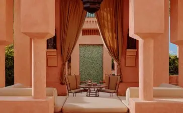 Villa 37 courtyard at Amanjena, Morocco, with symmetrical terracotta archways and draped curtains framing a seating area.