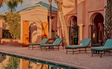 Villa terrace at Amanjena with ochre-coloured walls, lounge chairs, and palm trees in Morocco.