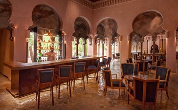 Amanjena's bar fumoir with terracotta walls, arched windows, and wooden seating areas lit by warm ambient light.