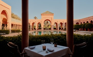 Amanjena's courtyard at dusk, with arched ochre architecture framing a central garden and dining table.
