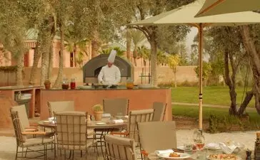 Olive grove terrace at Amanjena resort with dining tables, chairs and umbrellas.