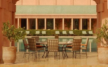 Amanjena's pool terrace restaurant with striped awning, dining tables and terracotta walls, Morocco.