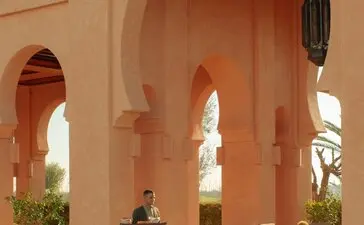 Piscine principale d'Amanjena, resort au Maroc, avec arches terracotta et bassin tranquille.