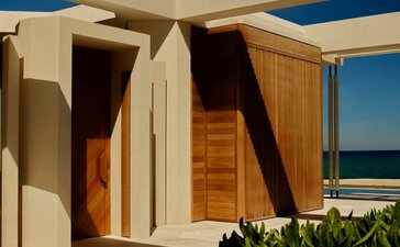 Beachfront casita with wooden doors and cream walls beneath a blue sky at Amanvari, Mexico.