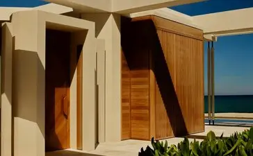 Beachfront casita with wooden doors and cream walls beneath a blue sky at Amanvari, Mexico.
