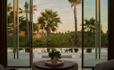 Interior view of Estuary Casita at Amanvari, Mexico, showing open glass doors framing palm trees and estuary landscape at dusk.