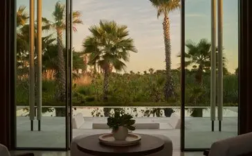 Interior view of Estuary Casita at Amanvari, Mexico, showing open glass doors framing palm trees and estuary landscape at dusk.
