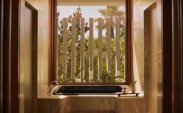 Bathroom in a Horizon Casita at Amanvari, Mexico, with a deep soaking tub positioned beneath a window framing views of desert landscape and cacti.