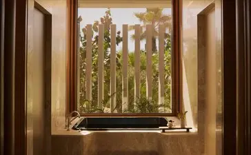 Bathroom in a Horizon Casita at Amanvari, Mexico, with a deep soaking tub positioned beneath a window framing views of desert landscape and cacti.