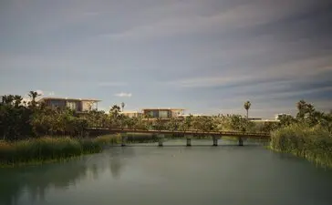 Horizon Casita at Amanvari overlooks a tranquil river with distant buildings and palm trees under a soft sky.