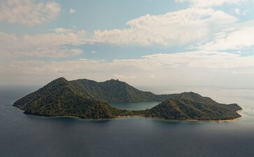 Drone view of Satonda Island's volcanic landscape rising from calm waters at Amanwana, Indonesia.